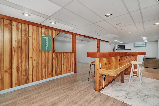 interior space featuring indoor bar, a paneled ceiling, wooden walls, and light hardwood / wood-style floors