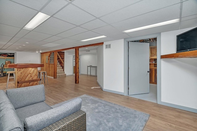 living room featuring bar area, a drop ceiling, and light wood-type flooring