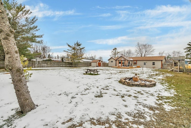 yard covered in snow with an outdoor fire pit, a playground, and a shed