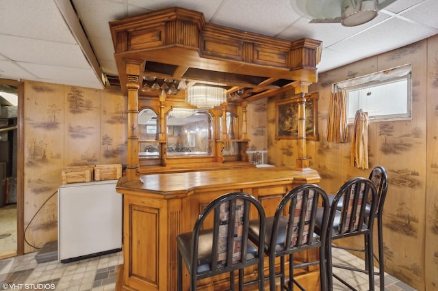 bar with wood counters, wooden walls, and a drop ceiling