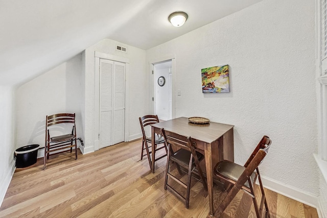 dining area featuring light wood-type flooring and vaulted ceiling