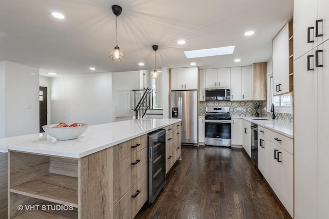 kitchen featuring a large island, sink, pendant lighting, stainless steel appliances, and beverage cooler