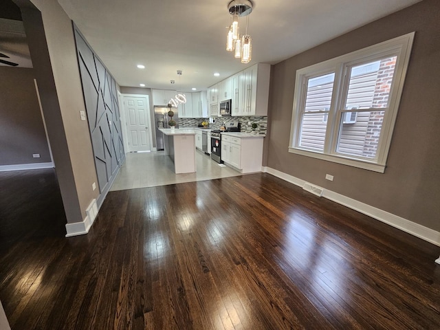 kitchen with a center island, white cabinetry, stainless steel appliances, decorative backsplash, and hanging light fixtures