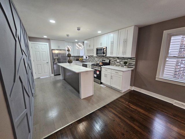 kitchen featuring hardwood / wood-style floors, a center island, white cabinetry, hanging light fixtures, and appliances with stainless steel finishes