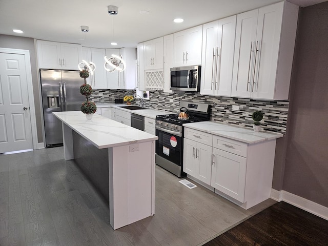 kitchen featuring white cabinets, a center island, stainless steel appliances, sink, and hanging light fixtures