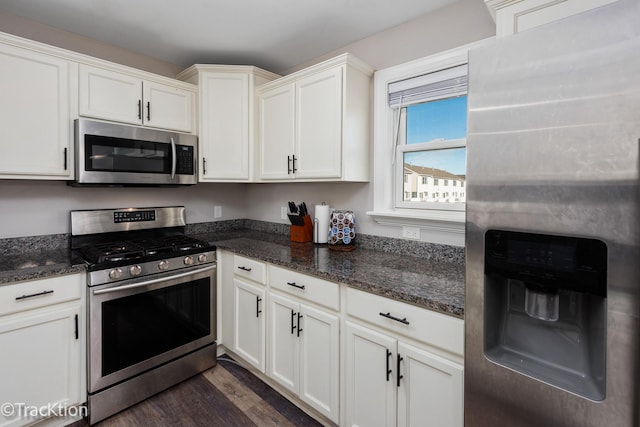 kitchen with white cabinets, stainless steel appliances, dark stone counters, and dark wood-type flooring