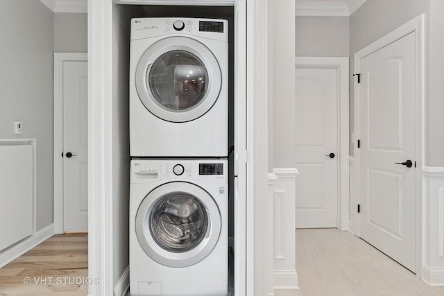 laundry room featuring stacked washer / dryer, ornamental molding, and light wood-type flooring