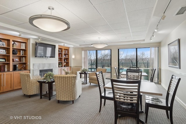 carpeted dining area with a tiled fireplace, built in features, and rail lighting