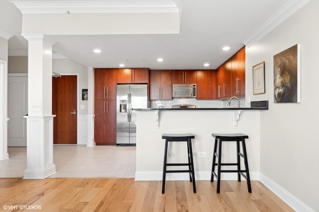 kitchen featuring a kitchen bar, ornate columns, appliances with stainless steel finishes, kitchen peninsula, and light hardwood / wood-style floors