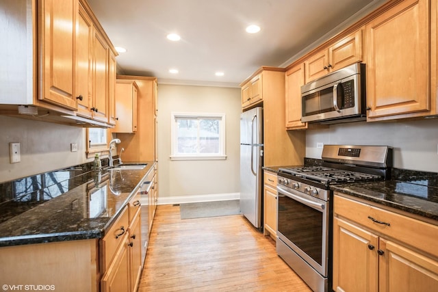 kitchen with stainless steel appliances, sink, light hardwood / wood-style floors, and dark stone counters