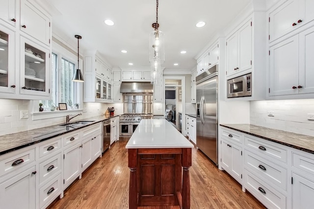 kitchen featuring decorative light fixtures, a kitchen island, sink, built in appliances, and hardwood / wood-style flooring