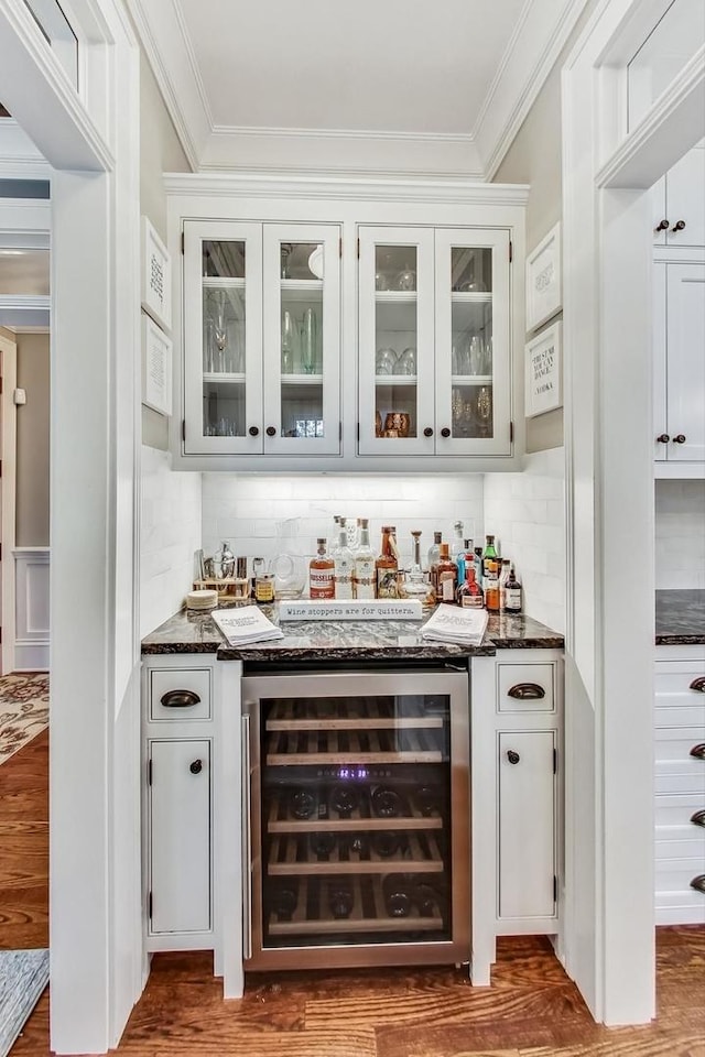 bar with white cabinets, dark hardwood / wood-style flooring, dark stone counters, wine cooler, and ornamental molding