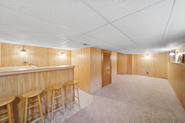 bar with a drop ceiling, carpet, and wood walls