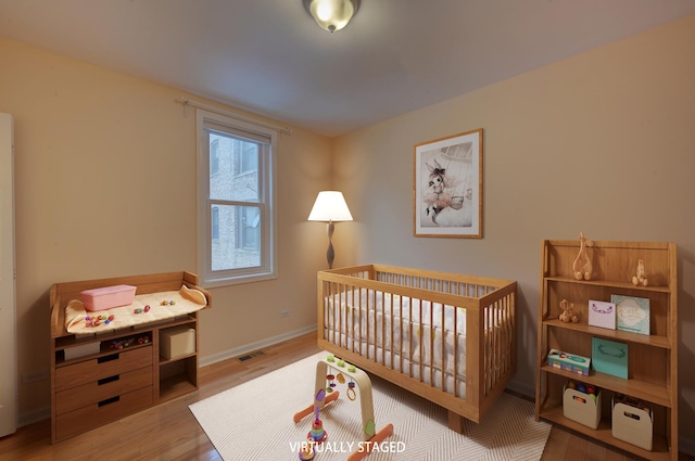 bedroom featuring light wood-type flooring and a nursery area