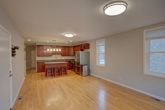 kitchen featuring pendant lighting, a center island, a kitchen bar, stainless steel appliances, and light hardwood / wood-style floors