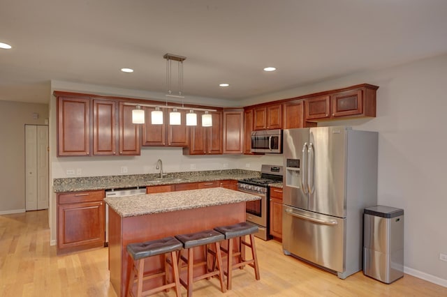 kitchen featuring pendant lighting, a kitchen island, a kitchen bar, stainless steel appliances, and light hardwood / wood-style flooring