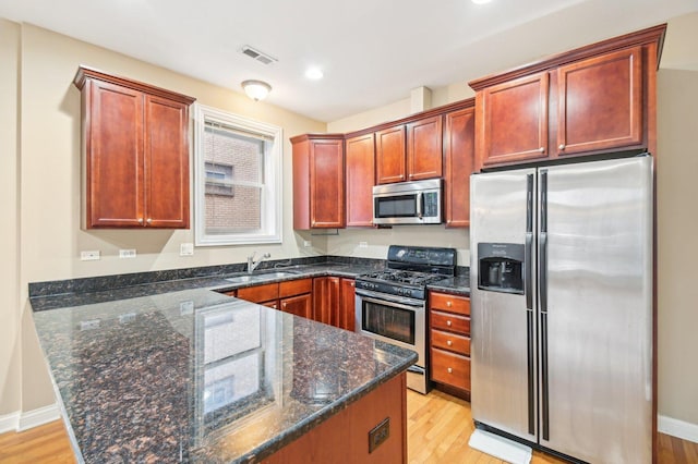 kitchen with appliances with stainless steel finishes, sink, light hardwood / wood-style floors, and dark stone counters