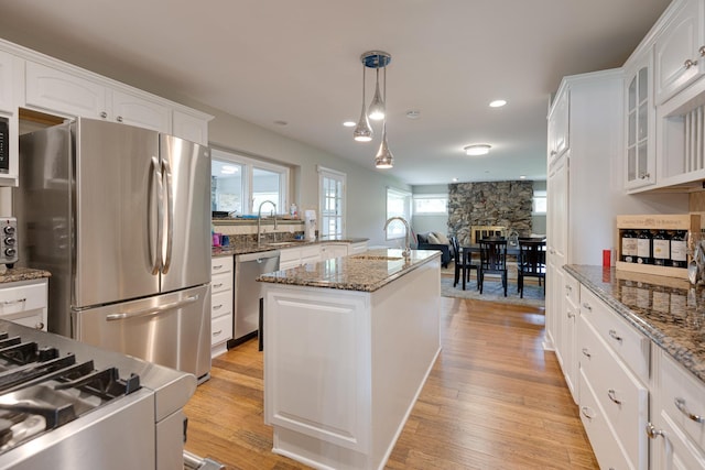 kitchen with pendant lighting, appliances with stainless steel finishes, a center island, white cabinets, and dark stone counters