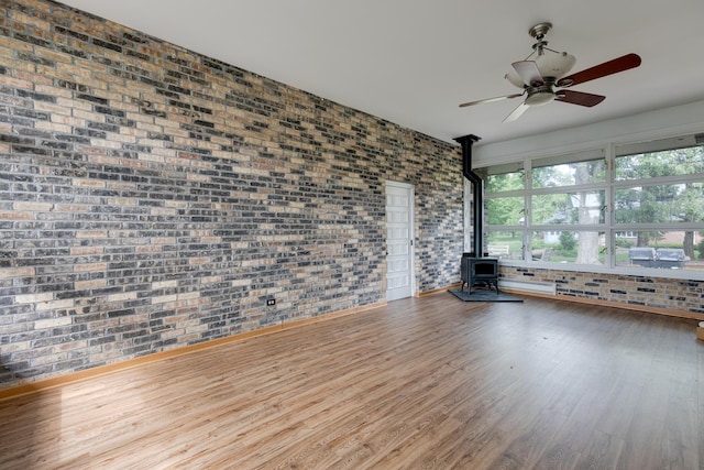 unfurnished living room featuring ceiling fan, brick wall, wood-type flooring, and a wood stove