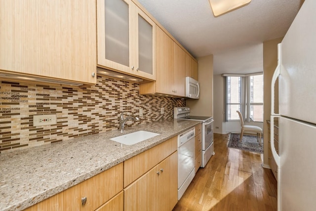 kitchen featuring light stone countertops, white appliances, light brown cabinets, decorative backsplash, and sink