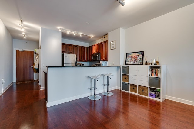 kitchen with rail lighting, appliances with stainless steel finishes, dark hardwood / wood-style floors, and kitchen peninsula