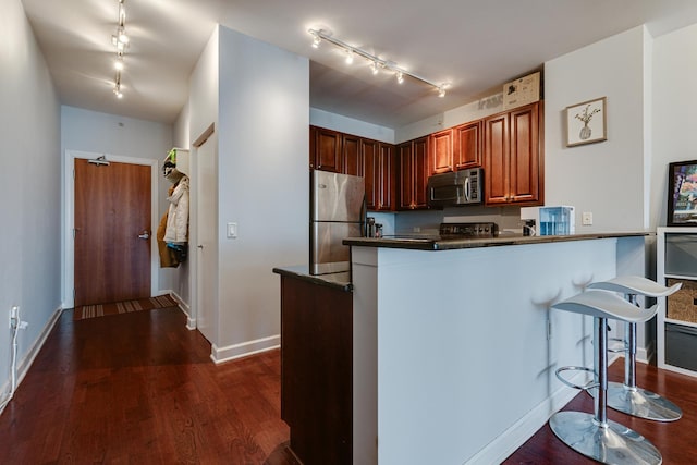 kitchen with a kitchen bar, track lighting, dark hardwood / wood-style floors, kitchen peninsula, and stainless steel appliances