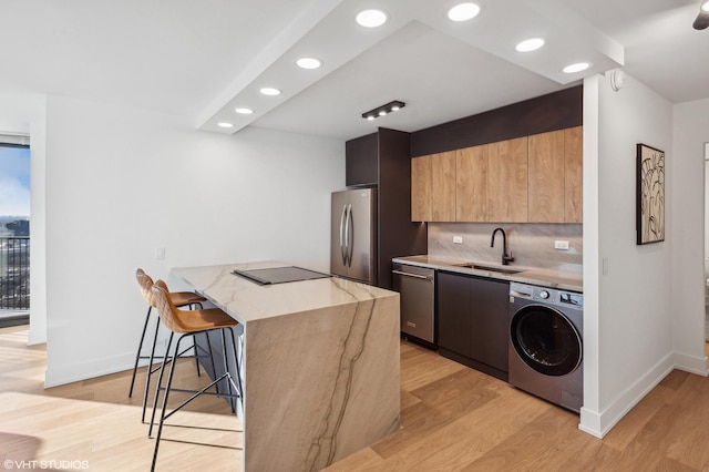 kitchen with washer / clothes dryer, appliances with stainless steel finishes, sink, light hardwood / wood-style flooring, and a breakfast bar