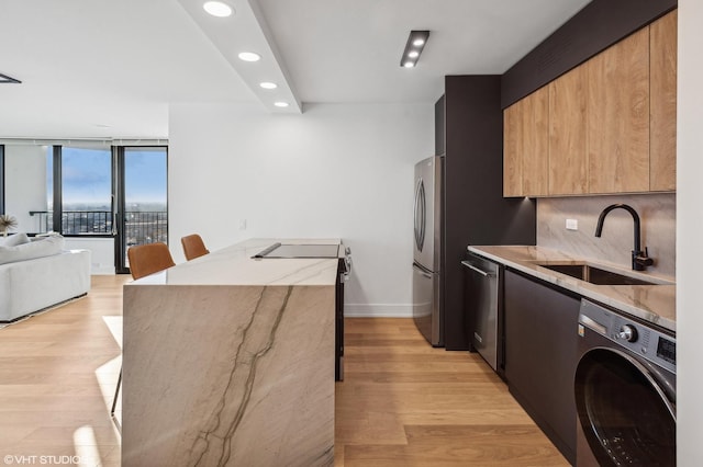 kitchen with washer / dryer, light hardwood / wood-style flooring, decorative backsplash, sink, and expansive windows