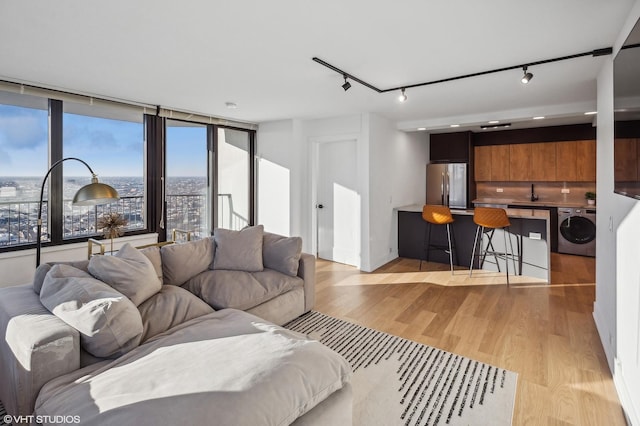 living room with rail lighting, washer / clothes dryer, light wood-type flooring, and a healthy amount of sunlight