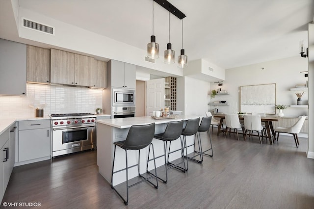 kitchen with tasteful backsplash, hanging light fixtures, a breakfast bar area, stainless steel appliances, and dark hardwood / wood-style flooring