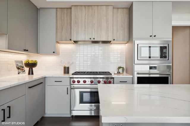 kitchen with stainless steel appliances, backsplash, light brown cabinetry, light stone countertops, and range hood