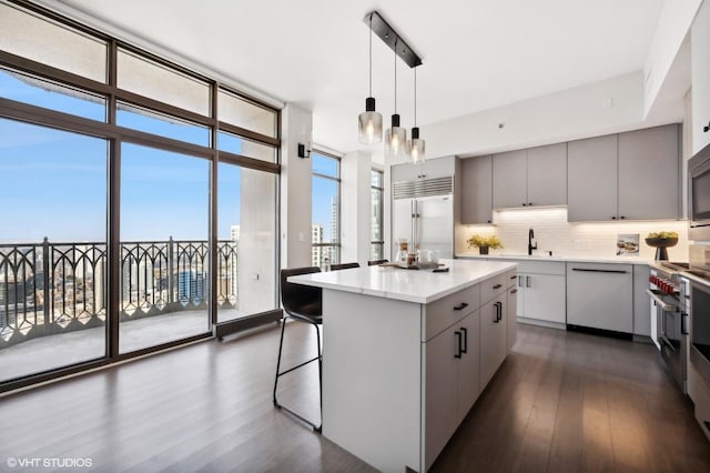 kitchen featuring appliances with stainless steel finishes, gray cabinetry, decorative light fixtures, expansive windows, and a center island