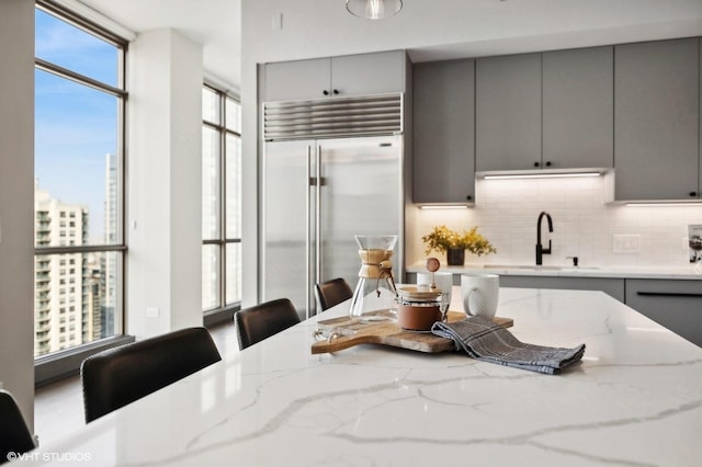 kitchen featuring built in refrigerator, a kitchen breakfast bar, light stone counters, and gray cabinetry