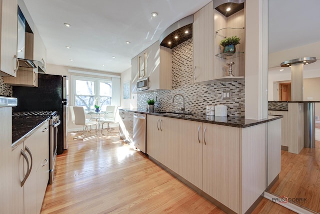 kitchen featuring sink, light hardwood / wood-style flooring, dark stone countertops, appliances with stainless steel finishes, and decorative backsplash