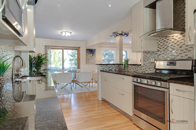 kitchen featuring appliances with stainless steel finishes, sink, dark stone countertops, backsplash, and wall chimney range hood