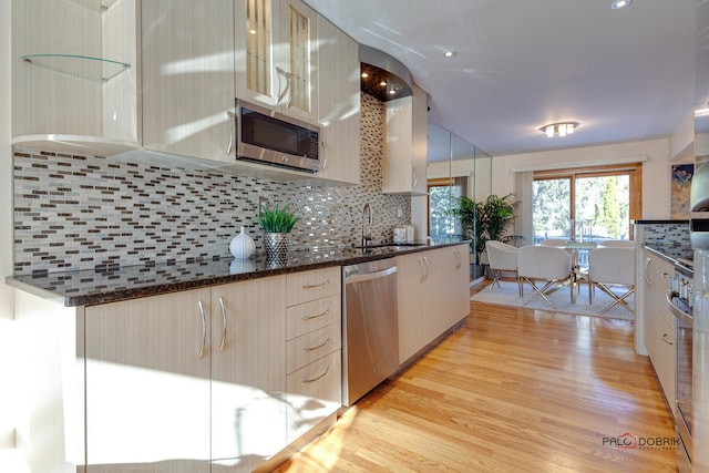 kitchen featuring sink, tasteful backsplash, light wood-type flooring, dark stone countertops, and appliances with stainless steel finishes