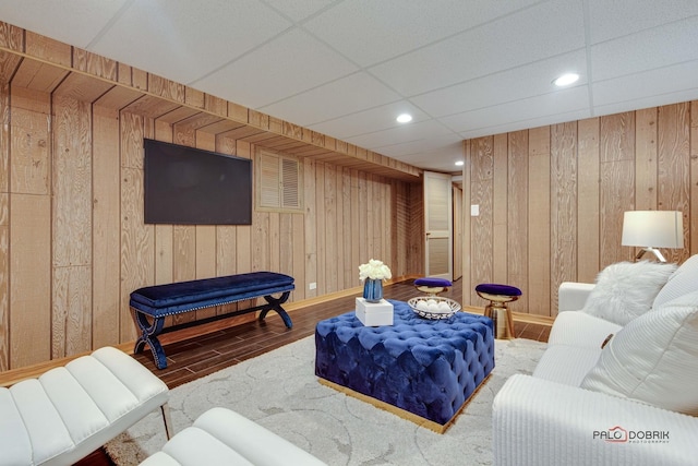 living room with wood-type flooring, a paneled ceiling, and wood walls