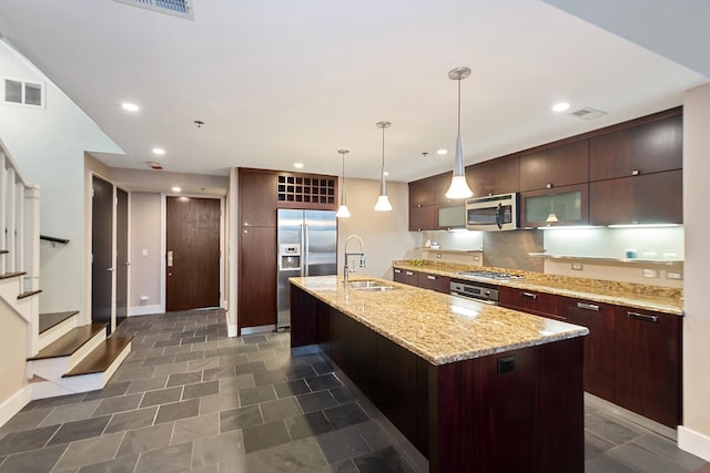 kitchen with an island with sink, sink, hanging light fixtures, dark brown cabinetry, and stainless steel appliances