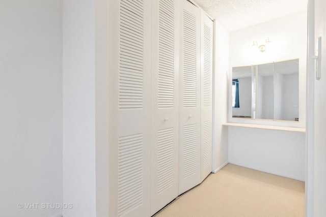 hallway with light carpet and a textured ceiling