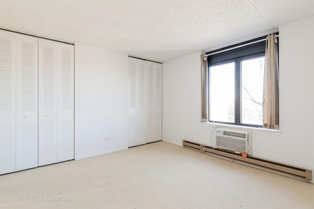 unfurnished bedroom featuring two closets, a baseboard radiator, a wall mounted AC, light colored carpet, and a textured ceiling