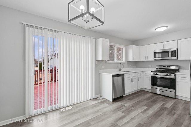 kitchen featuring sink, white cabinetry, light hardwood / wood-style flooring, pendant lighting, and stainless steel appliances