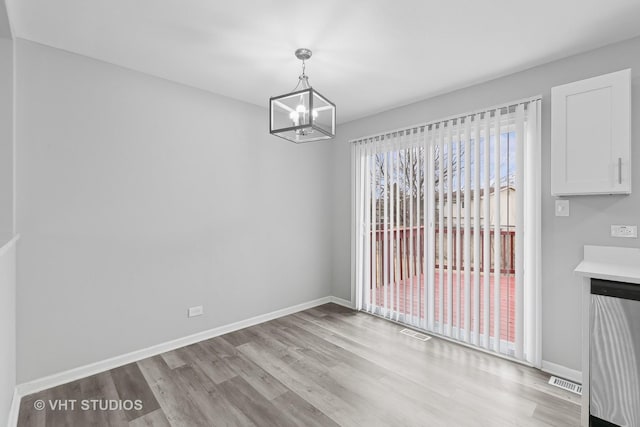 unfurnished dining area featuring an inviting chandelier and light hardwood / wood-style floors