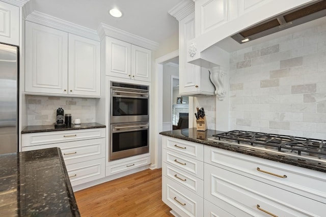 kitchen featuring white cabinetry, stainless steel appliances, tasteful backsplash, dark stone counters, and light wood-type flooring