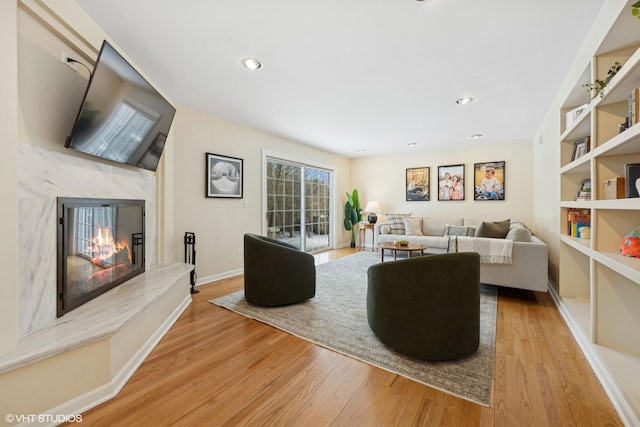 living room with built in shelves, light hardwood / wood-style floors, and a premium fireplace