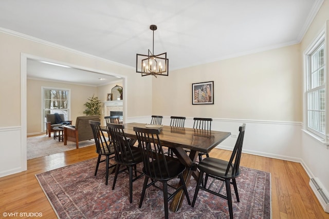 dining area with an inviting chandelier, a baseboard heating unit, crown molding, and light hardwood / wood-style flooring