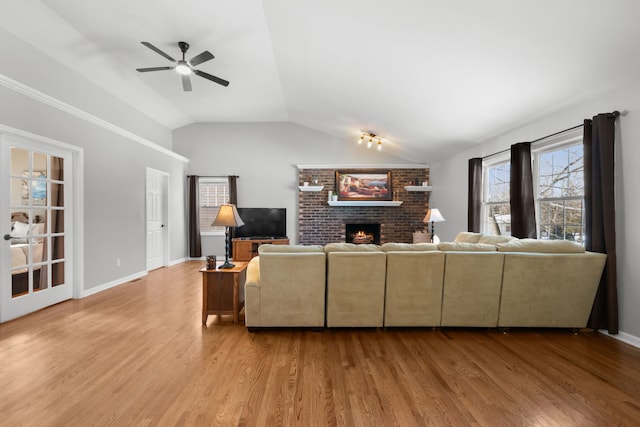 living room with vaulted ceiling, a brick fireplace, light hardwood / wood-style flooring, and ceiling fan