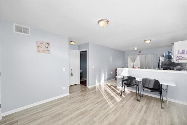 kitchen with stainless steel fridge, white cabinetry, and light hardwood / wood-style flooring