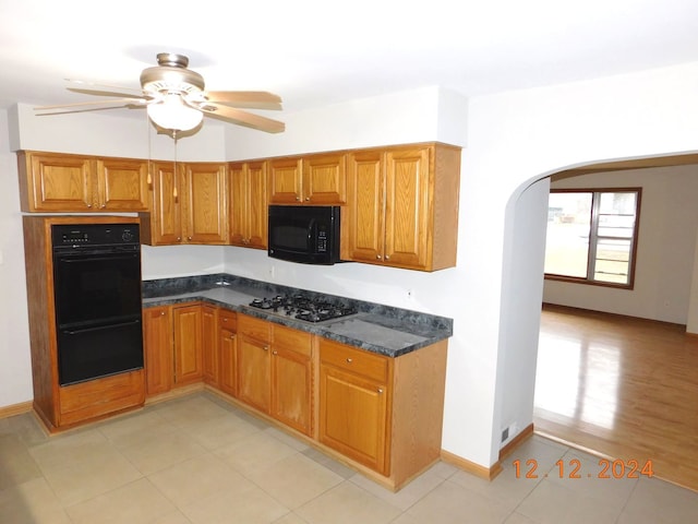 kitchen featuring dark stone countertops, light tile patterned floors, black appliances, and ceiling fan