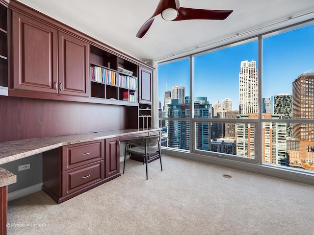 office space with ceiling fan, expansive windows, light carpet, and built in desk