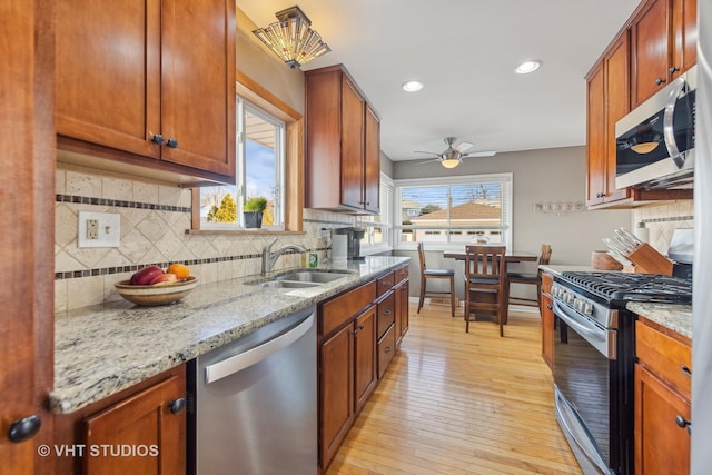 kitchen with appliances with stainless steel finishes, tasteful backsplash, sink, light hardwood / wood-style floors, and light stone countertops